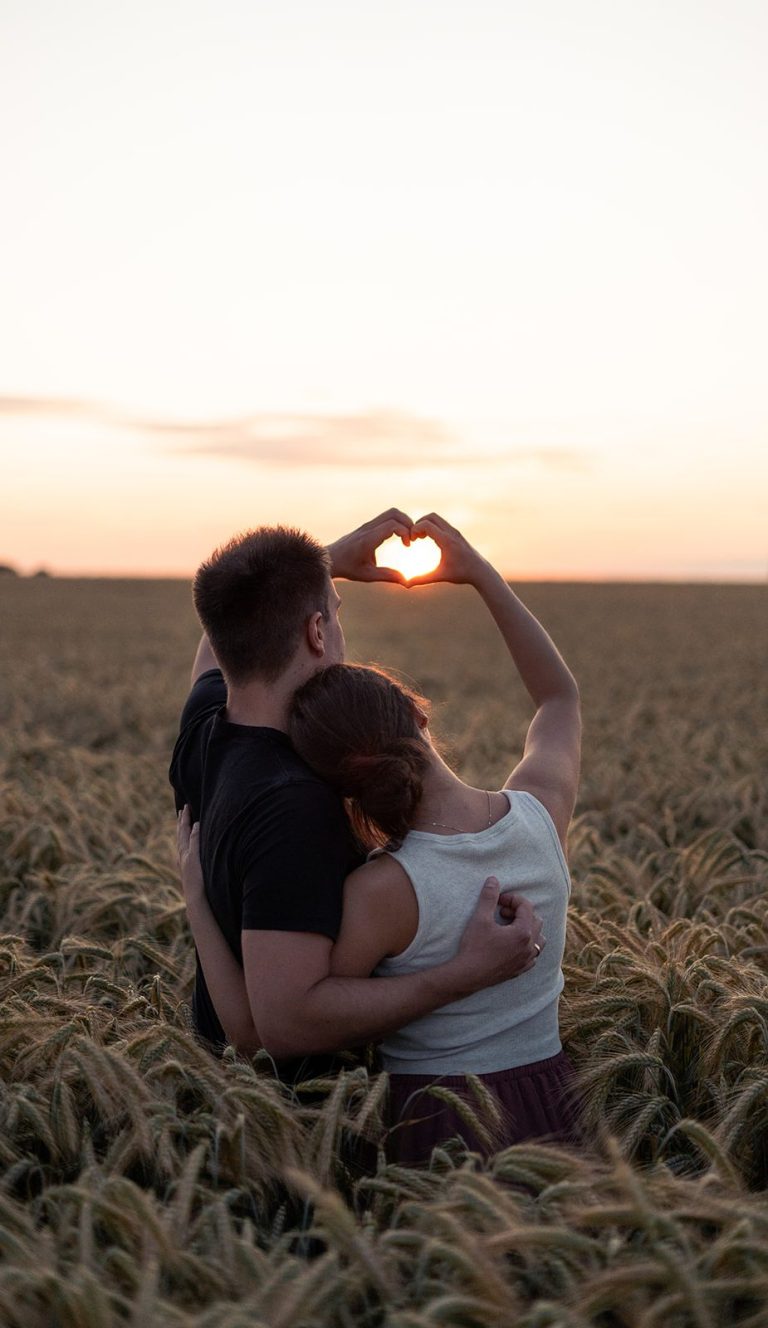 Ein Paar steht in einem Feld bei Sonnenuntergang, der Mann trägt die Frau auf dem Rücken.